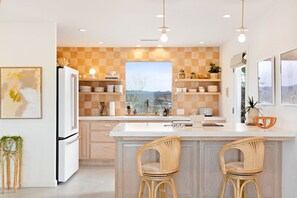 Une cuisine moderne avec un îlot central, des meubles blancs et une vue par la fenêtre.