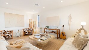A modern living room with a sofa, chairs, a coffee table, and a guitar.