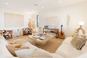 A modern living room with a sofa, chairs, a coffee table, and a guitar.