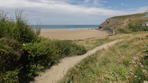 Uma trilha costeira que leva a uma praia, com vista clara para o mar e um penhasco.