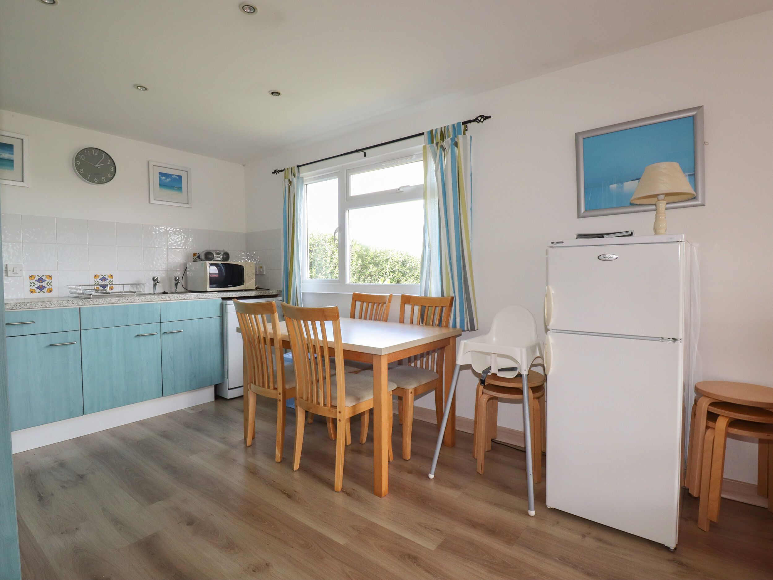 A compact kitchen with a dining area, wooden cabinets, a white refrigerator, and a window with curtains.