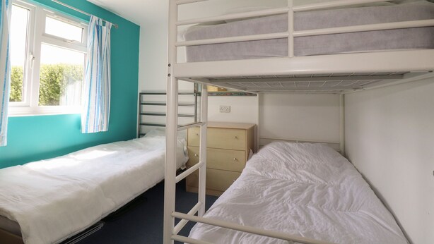 Quarto com beliches, janela com cortinas, cômoda e luminária no teto.