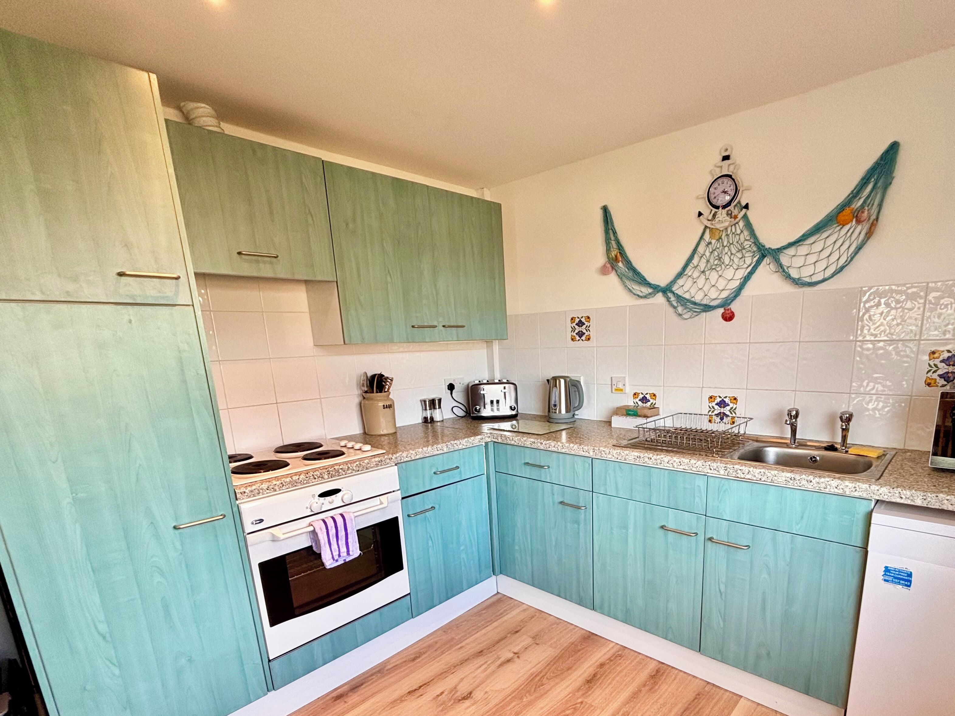 Een keuken met turquoise kastjes, een witte oven, een spoelbak en een decoratief net aan het aanrecht.