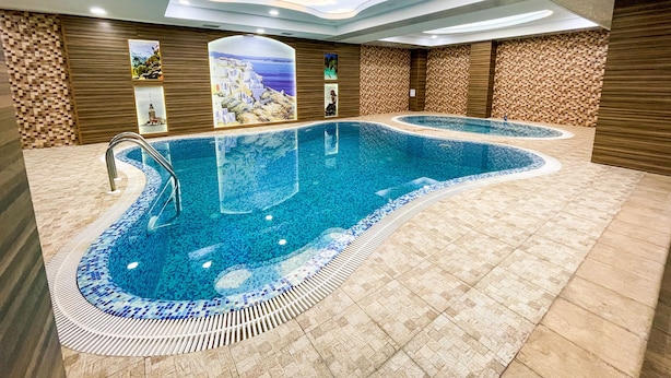 Une grande piscine intérieure dotée d’un plafond au design unique, d’un revêtement de sol en carrelage et de panneaux muraux décoratifs.