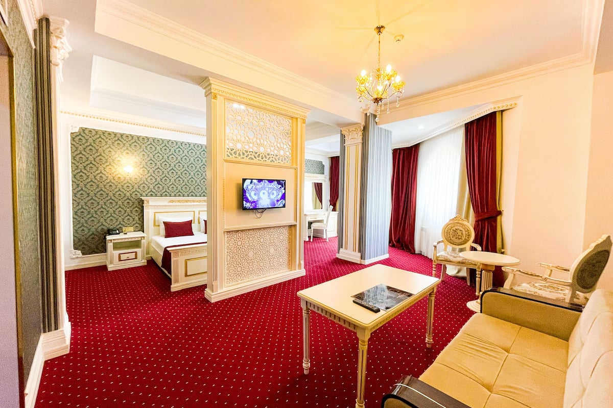 A hotel room with a red carpet, a bed, a TV, a sofa, and a table.