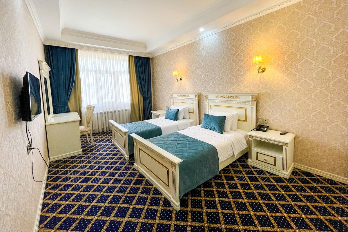 A hotel room with two beds, a television, a desk, and a patterned carpet.