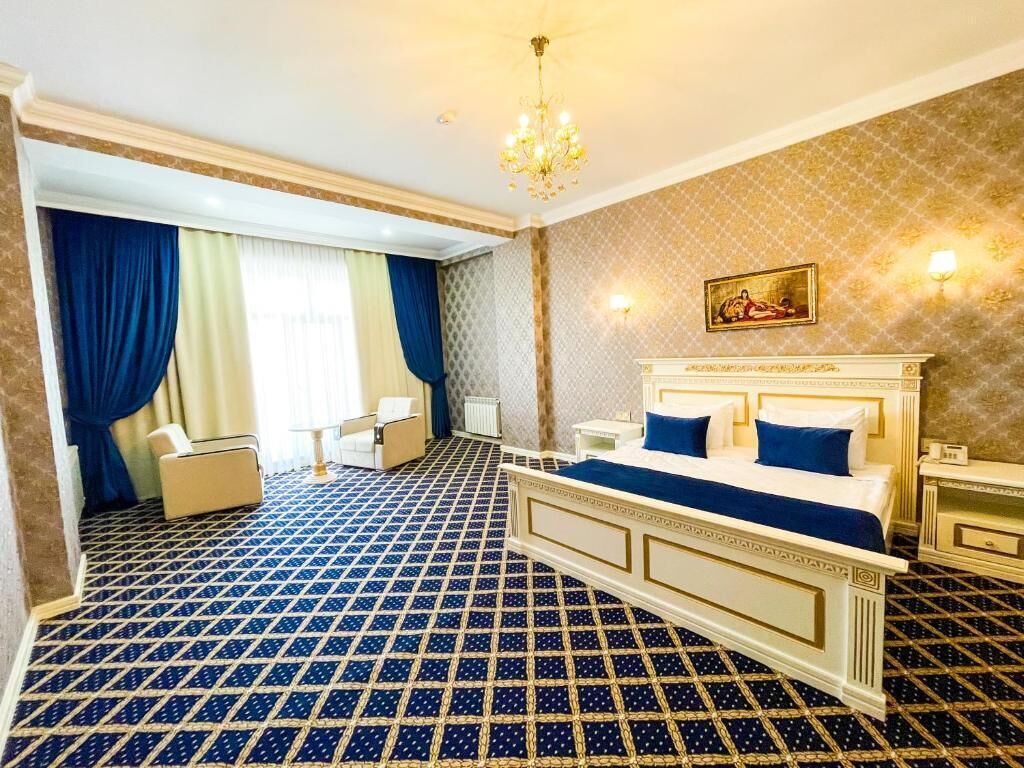 Une chambre d’hôtel avec un sol à motifs, un lit avec une literie bleue, un lustre et un tableau accroché au mur.