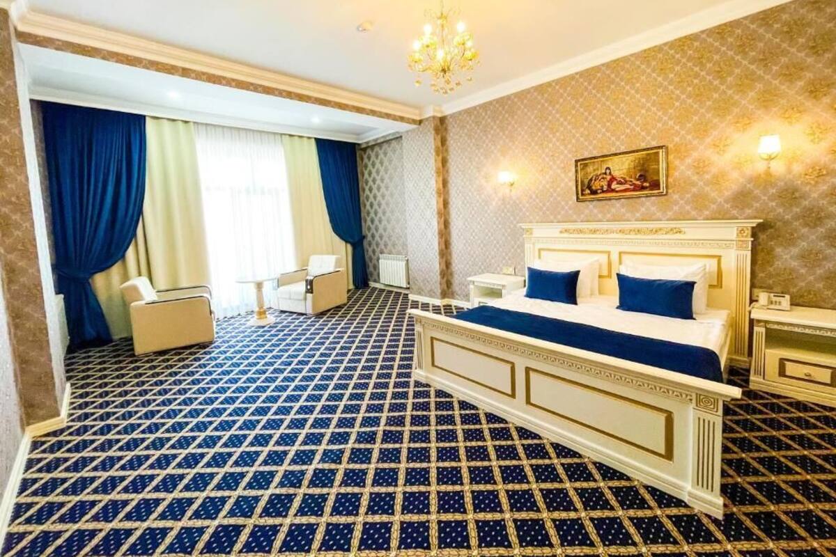 A hotel room with a patterned floor, a bed with blue bedding, a chandelier, and a painting on the wall.