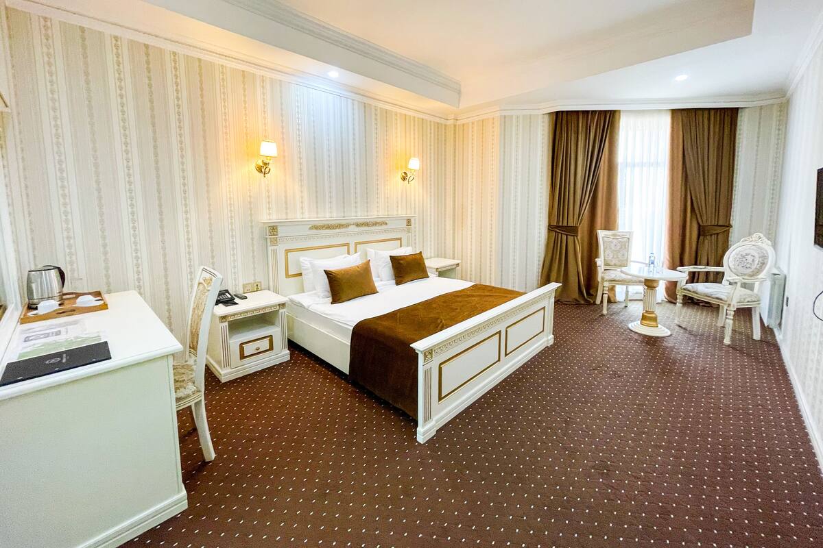 A hotel room with a large bed, two bedside tables, a desk, a chair, and a window with curtains.