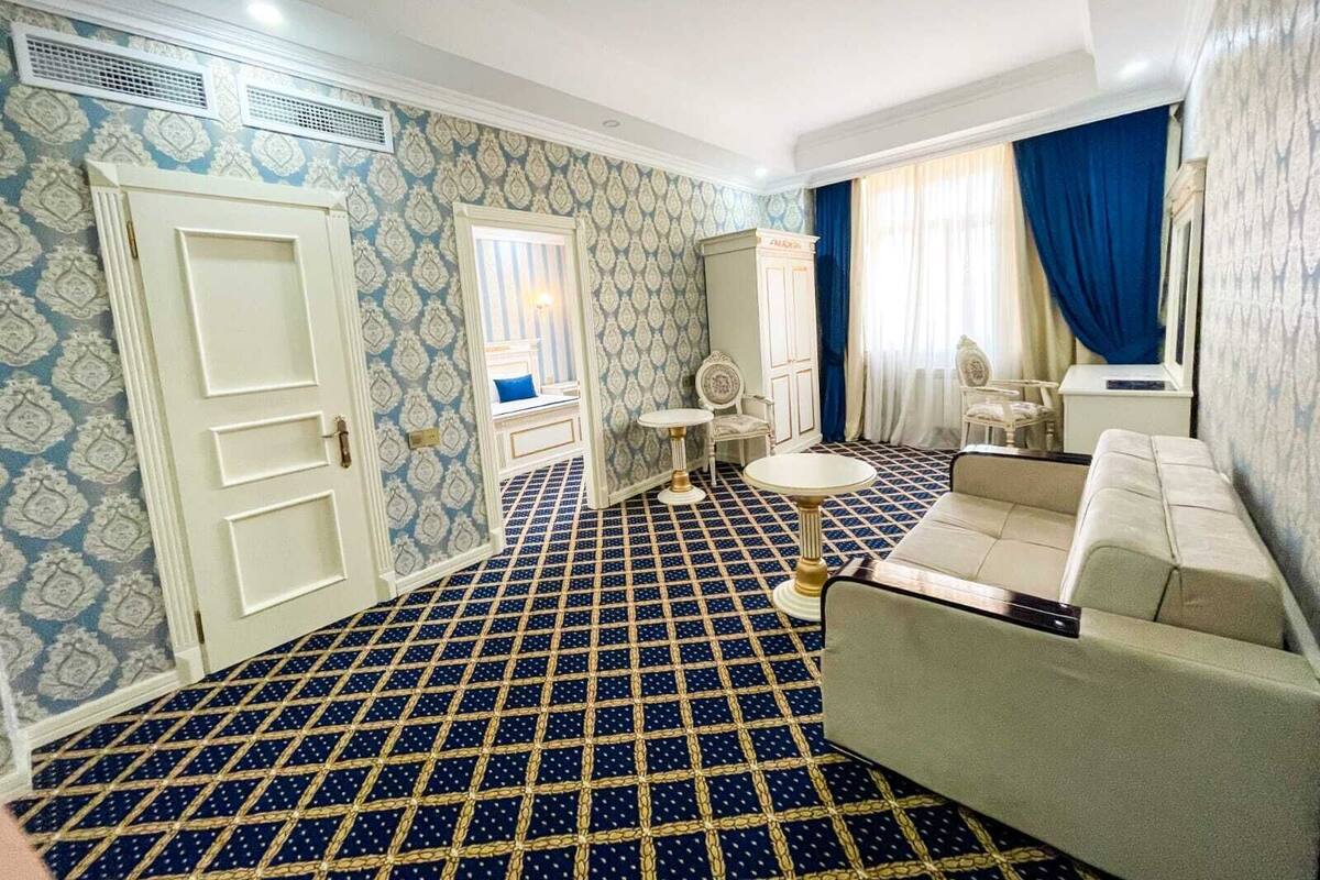 A room with a patterned floor, a sofa, a small table, a cabinet, and a window with curtains.