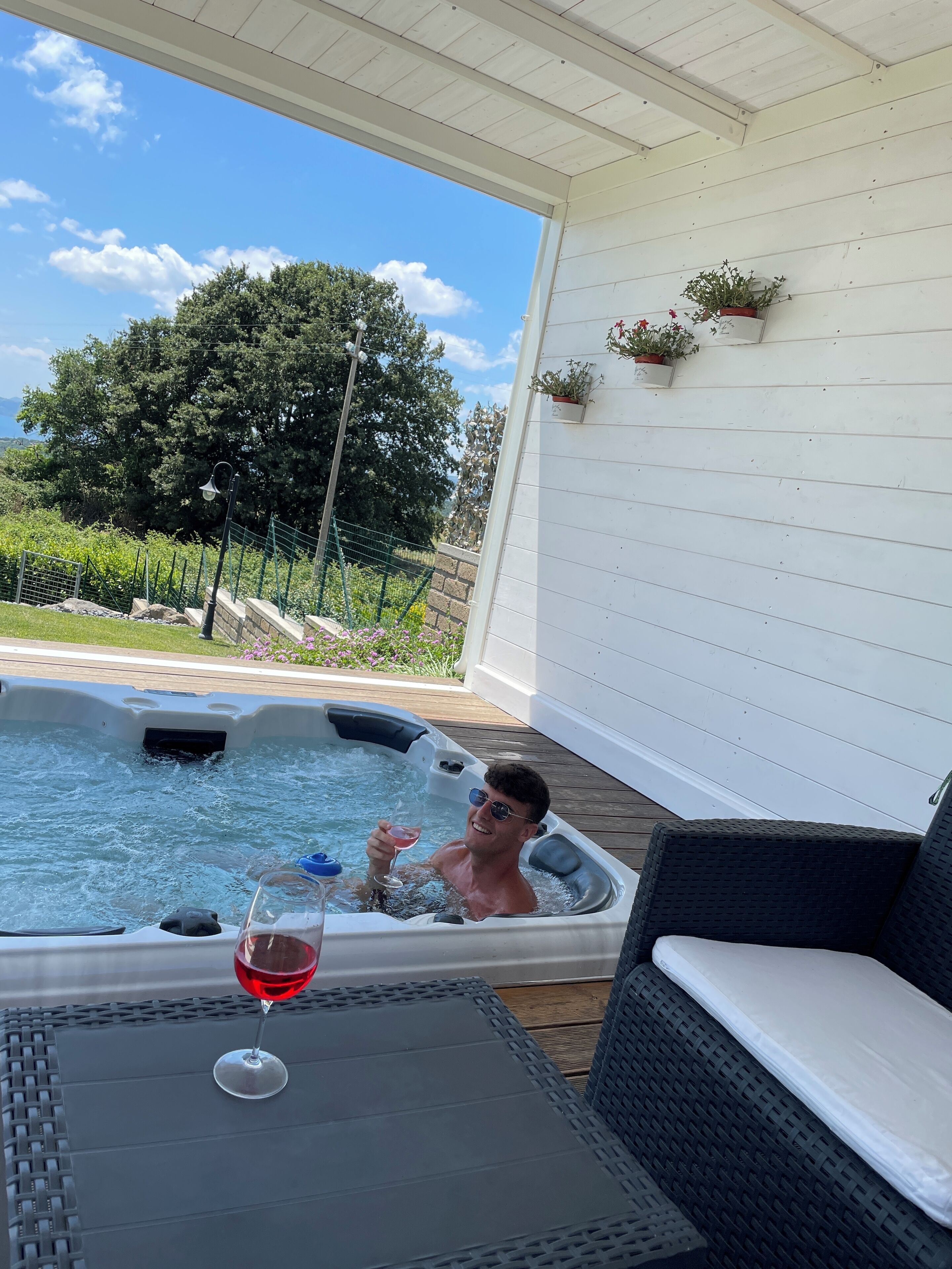 Un bain à remous avec une coupe de vin rouge posée sur une table, entouré de meubles en osier.