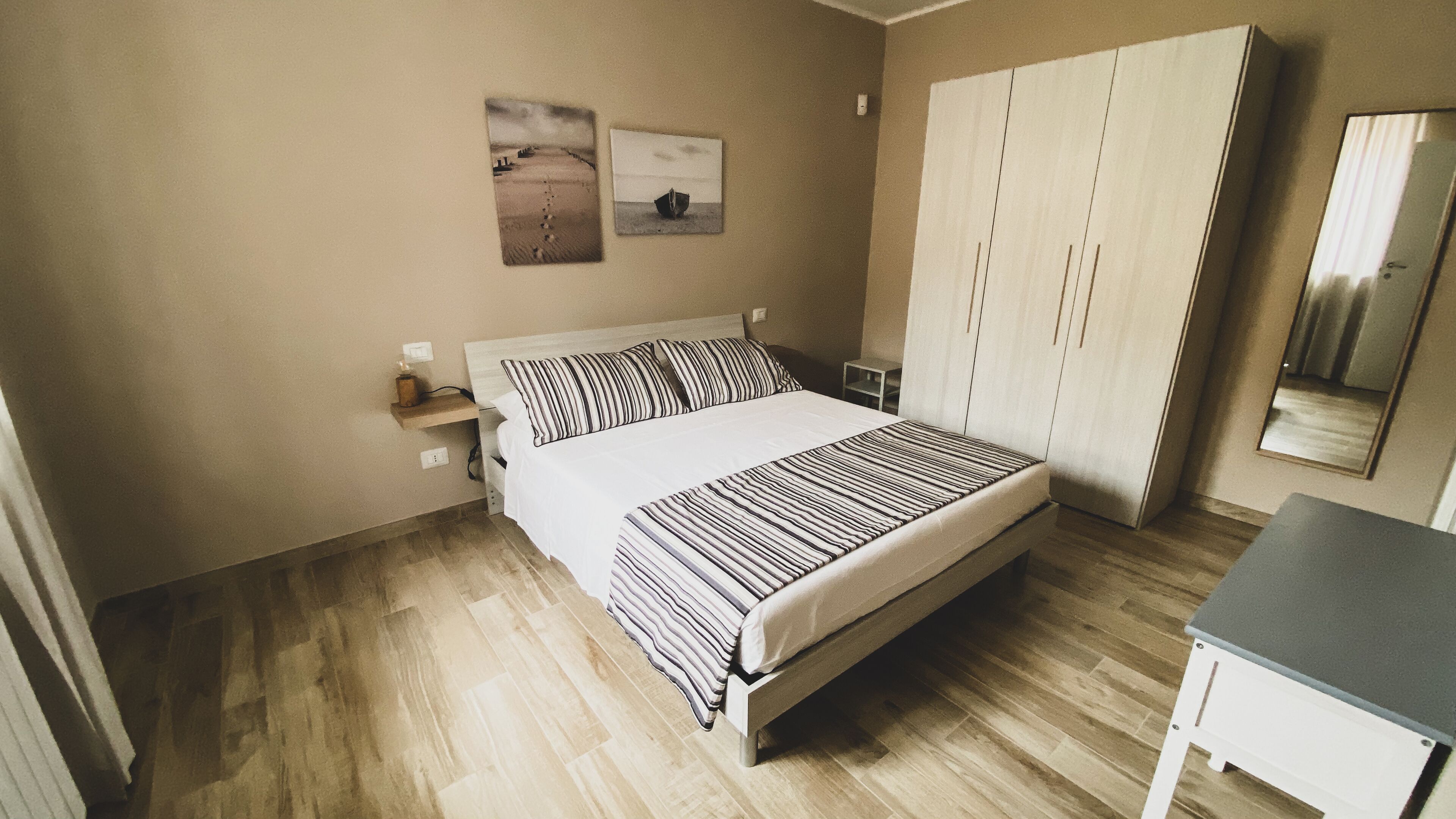 A bedroom with a bed, a wardrobe, a bedside table, and two wall-mounted pictures.
