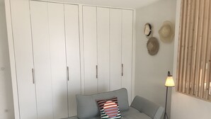 Una habitación con sofá gris, una mesita negra pequeña, una lámpara de pie y un armario blanco con líneas verticales.