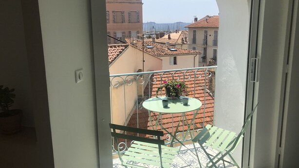 Un balcón con una mesa y sillas, una planta en maceta y vistas a edificios y un paisaje distante.