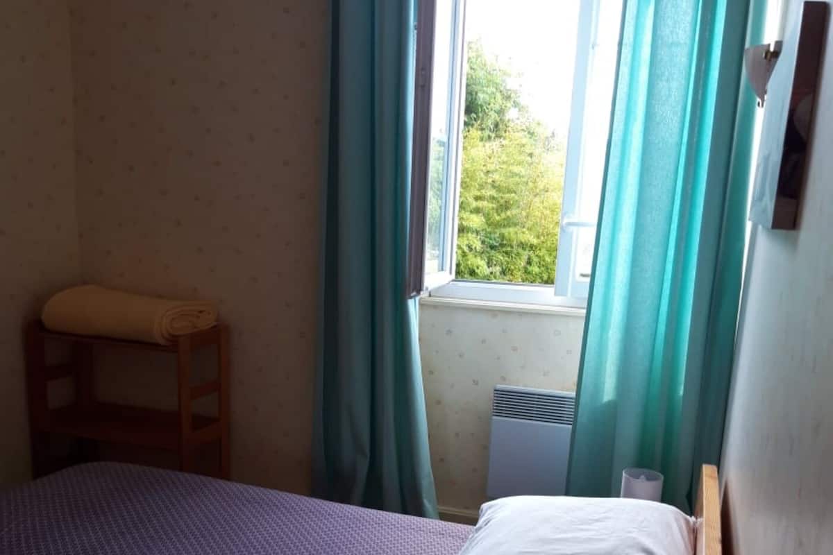 A small, single-bed room with a wooden ladder, a window with curtains, and a radiator.