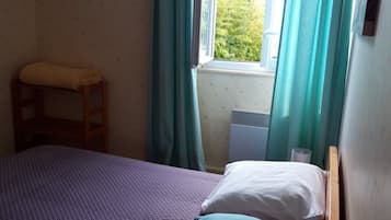 Une petite chambre avec un lit simple, une échelle en bois, une fenêtre avec des rideaux et un radiateur.