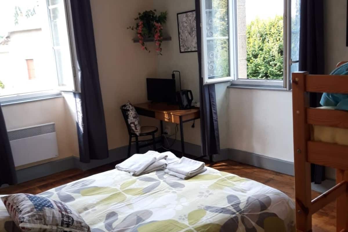 A bedroom with a bed, a desk, a chair, and a window with curtains.