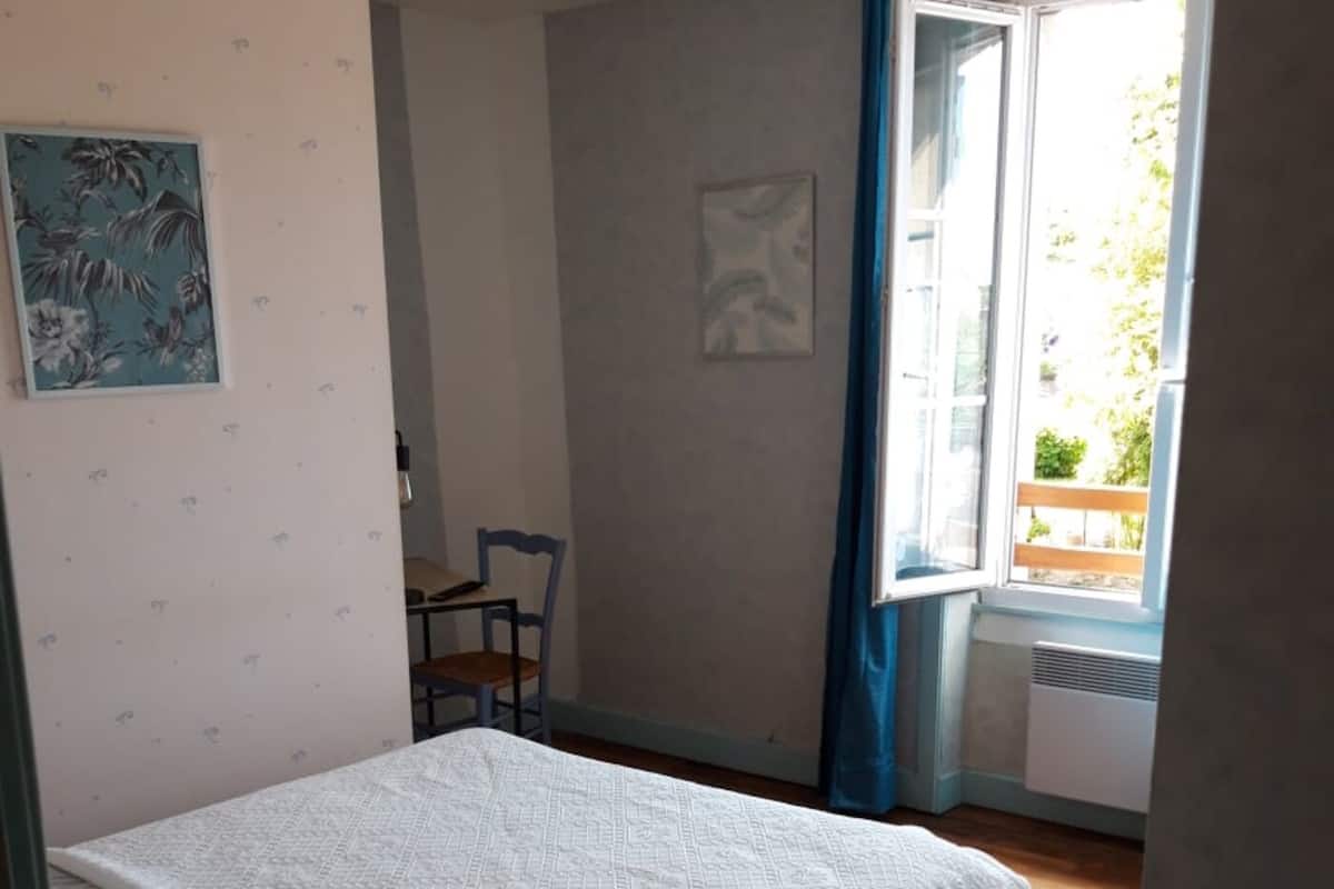 A bedroom with a bed, a chair, a window with curtains, and a radiator.