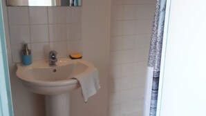 Une salle de bain avec un lavabo blanc, un miroir et un rideau de douche.