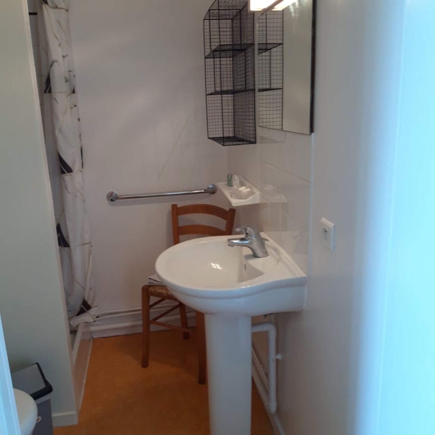 Un bagno piccolo con un lavandino bianco, una sedia di legno, un portasciugamani e una tenda da doccia.
