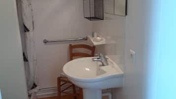 Un bagno piccolo con un lavandino bianco, una sedia di legno, un portasciugamani e una tenda da doccia.