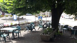 Un espace extérieur aménagé avec des tables et des chaises, situé sous un arbre et entouré d’une clôture.