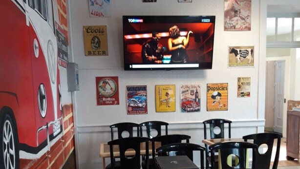 Un restaurant avec un téléviseur fixé au mur, diffusant un film, et décoré d’affiches anciennes.