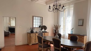A dining area with a round table, six chairs, a chandelier, and a fireplace in the background. - Town house with swimming pool and private garden (Pélissanne)