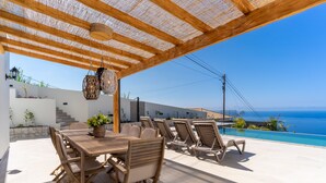 Une terrasse extérieure avec une table et des chaises en bois, une pergola agrémentée de guirlandes lumineuses et une vue sur la mer.