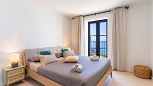 Une chambre moderne avec un grand lit, une table de chevet avec une lampe et une vue sur l’extérieur grâce à une grande fenêtre.