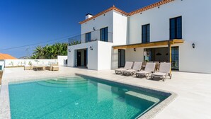 Une maison moderne à deux étages, dotée d’une piscine, d’un espace extérieur aménagé et surplombant un ciel d’un bleu éclatant.