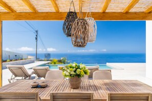 A wooden table with a woven basket of flowers, outdoor seating, and a view of the ocean. - Horizonte Azul (Ribeira Brava)