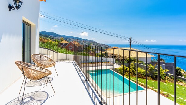 Un balcon avec une piscine, deux fauteuils en osier et une vue sur la mer et les collines.