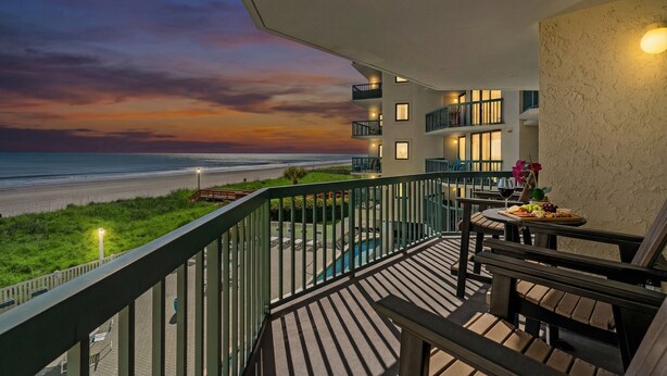 A balcony with a view of the beach at sunset, outdoor seating, and a pool. - Ocean Bay Club 202-4BR/3BA Oceanfront-Ocean Drive (North Myrtle Beach)