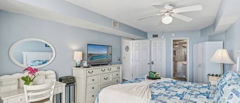 A bedroom with a bed, a desk, a chair, a television, and a ceiling fan.