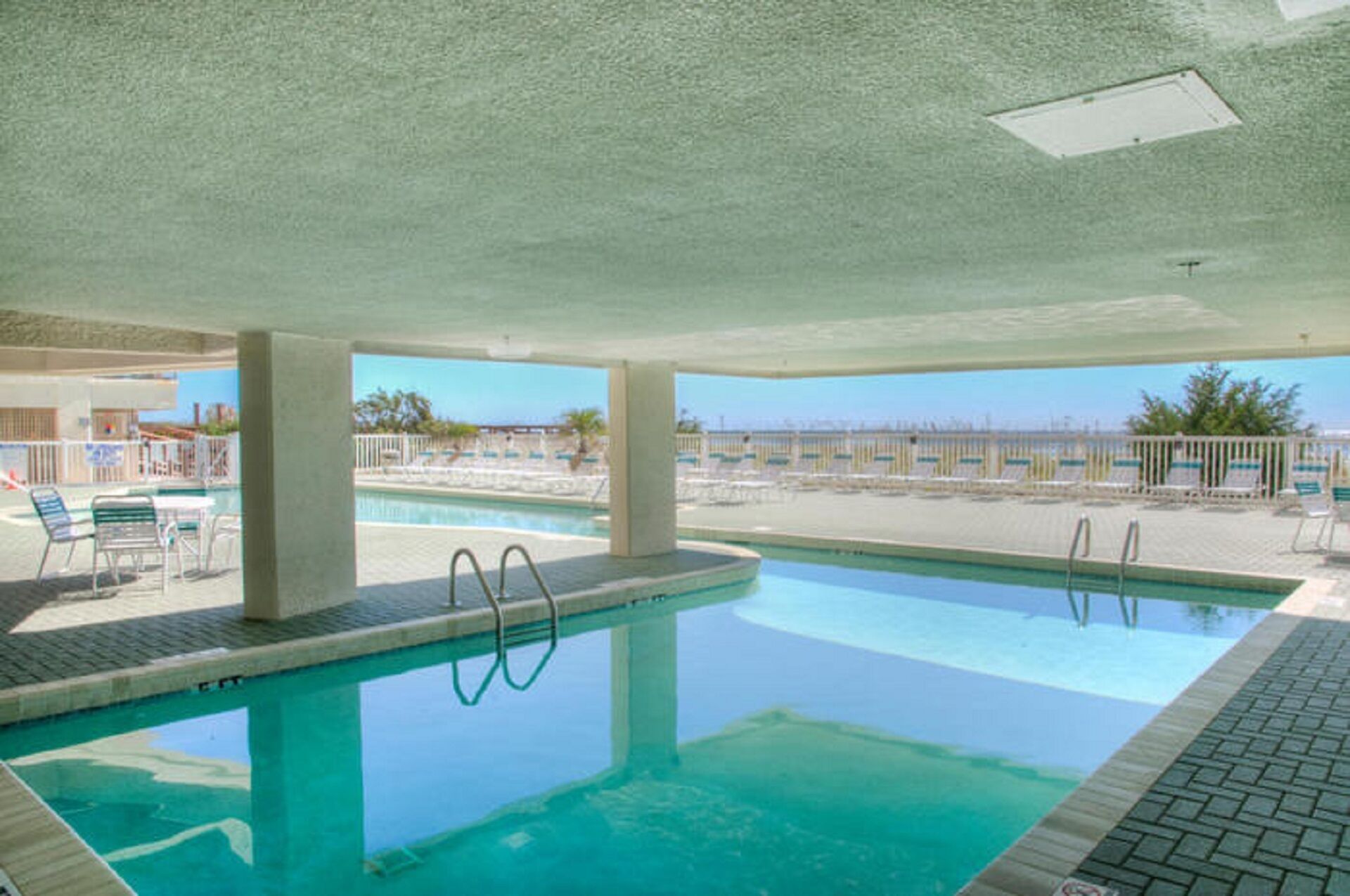 An indoor swimming pool with clear blue water, surrounded by lounge chairs and a view of the beach.