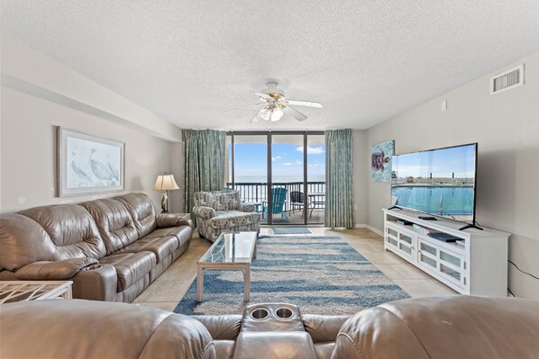 A living room with a leather sofa, a coffee table, a TV, and a view of the ocean through large windows.