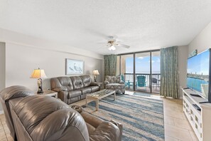 A spacious living room with a leather sofa, a coffee table, and a television on a stand.