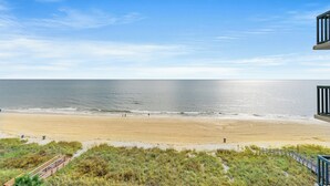 A beach view from a balcony with a wooden deck and a railing.