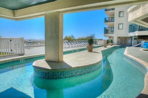 Ein Pool mit geschwungener Form, umgeben von einem weißen Zaun, und im Hintergrund ein Gebäude mit Balkonen.