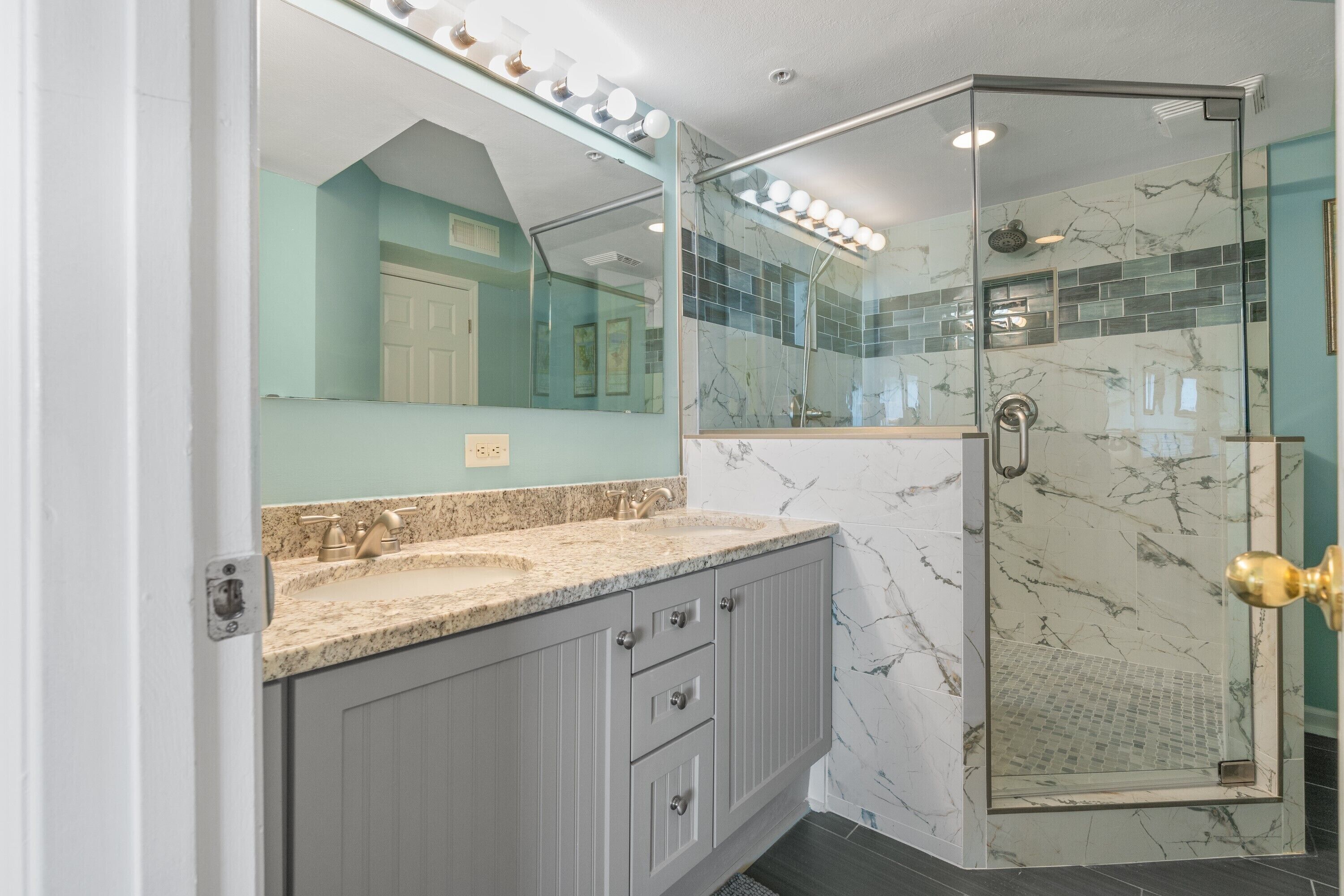 A bathroom with a vanity, a glass shower enclosure, and a large mirror with lights.