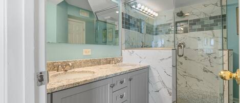 A bathroom with a vanity, a glass shower enclosure, and a large mirror with lights.
