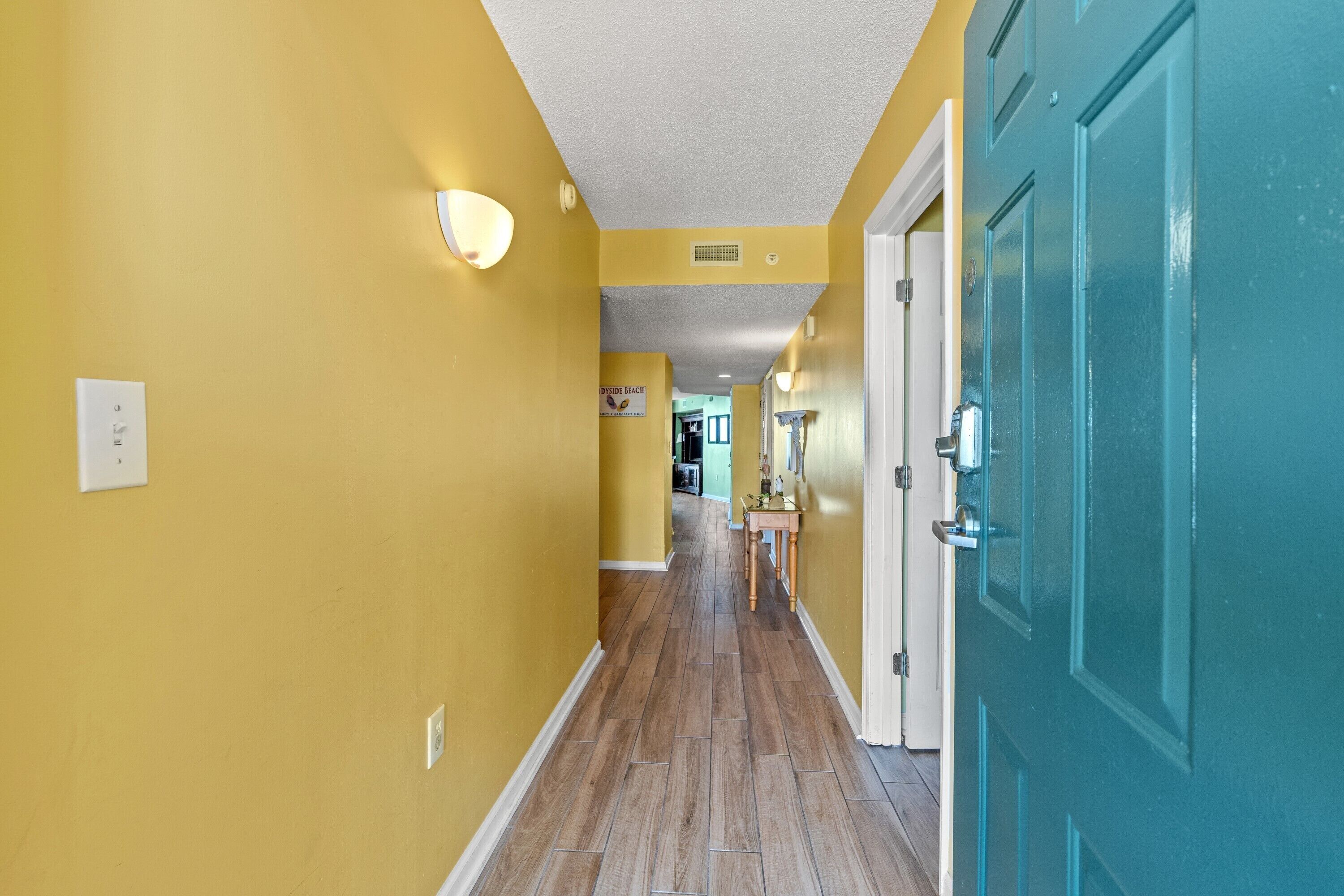 A hallway with yellow walls, wooden flooring, and teal doors.