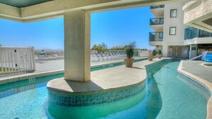 A swimming pool with a curved design, surrounded by a white fence, and a building with balconies in the background. - Ocean Bay Club 1605-4BR/3BA Oceanfront-Ocean Drive (North Myrtle Beach)