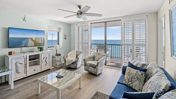 A spacious living room with a large TV, a ceiling fan, and a balcony with ocean views. - Ocean Bay Club 1605-4BR/3BA Oceanfront-Ocean Drive (North Myrtle Beach)