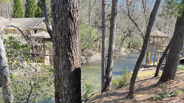 A rustic cabin with a stone pathway leading to a wooden deck overlooking a river.