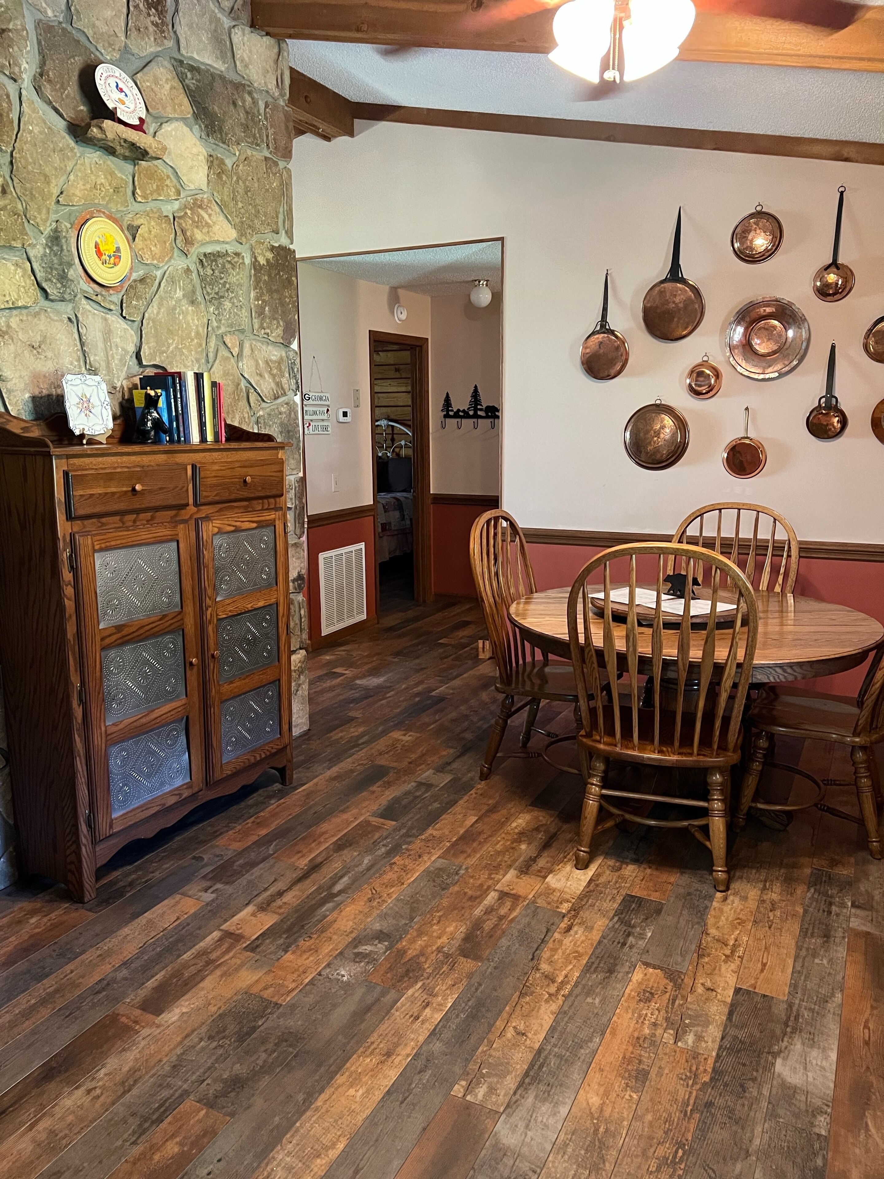 Un coin repas avec une table et des chaises en bois, un mur en pierre et une collection d’ustensiles de cuisine accrochés au mur.