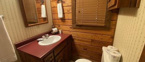 Un baño con paredes de madera, un lavabo, un espejo, un inodoro y una ventana con persianas.