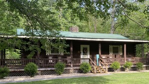 A rustic log cabin with a porch, wooden railings, and a green roof.