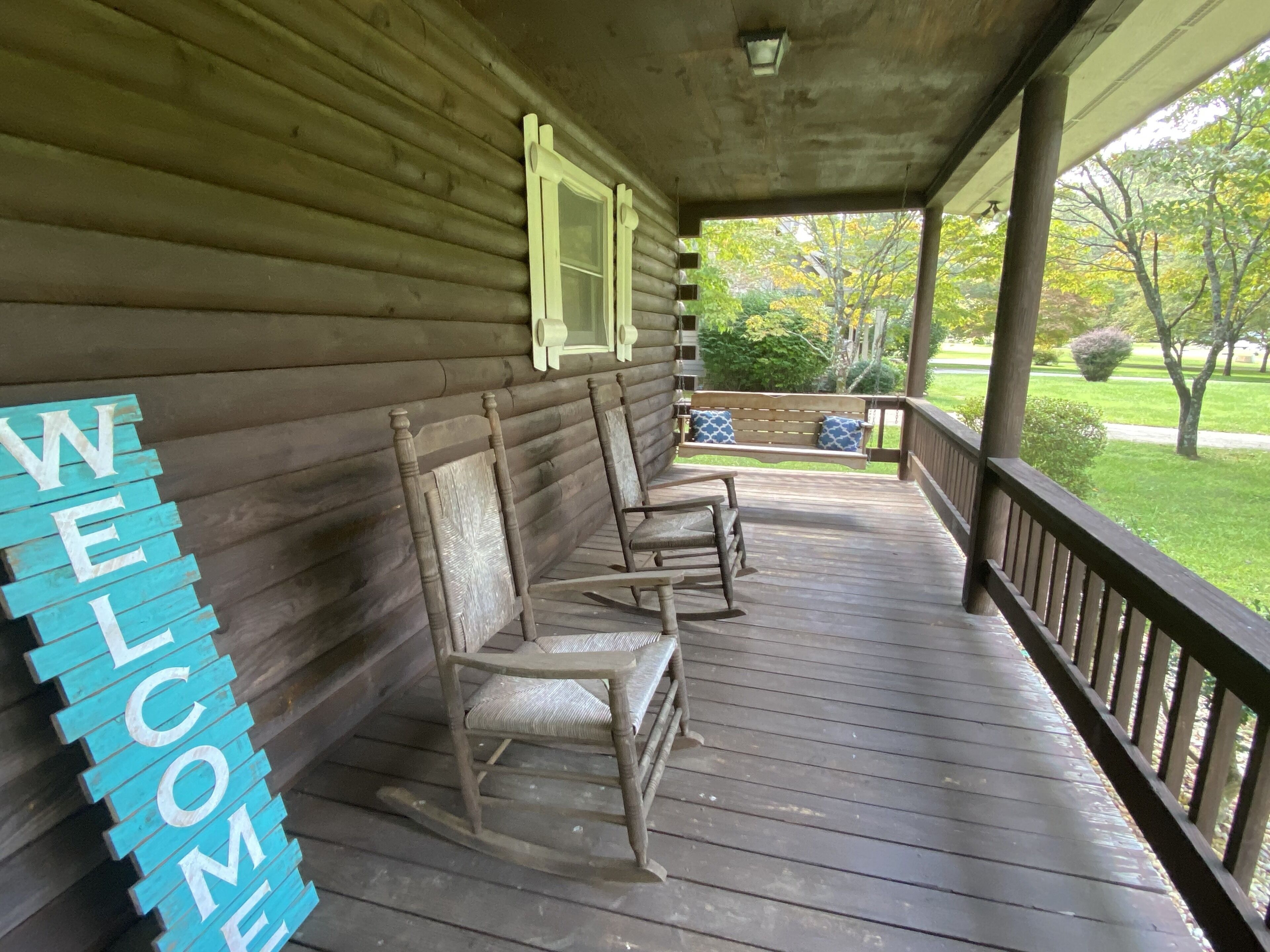 A wooden porch with rocking chairs and a 'WELCOME' sign.